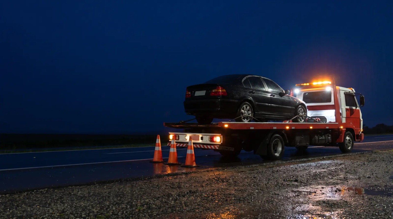 Guincho plataforma atendendo à noite na rodovia com cones de sinalização
